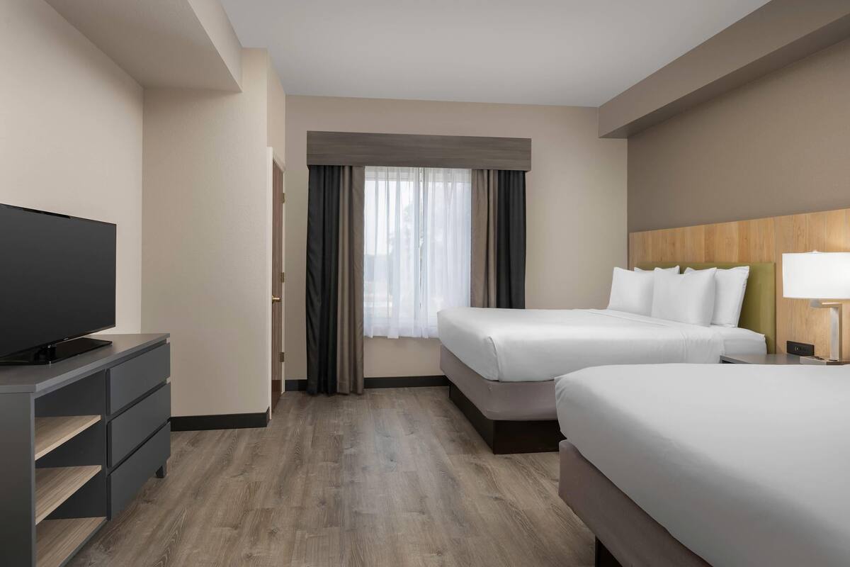 A hotel room with two beds, a TV, a desk, and a window with curtains.