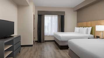 Habitación de hotel con dos camas, televisión, escritorio y ventana con cortinas.