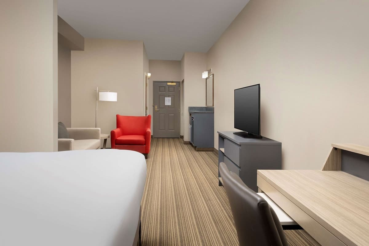 A hotel room with a bed, a desk, a television, a chair, and a door.
