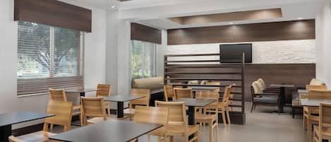 Un restaurant moderne avec des tables et des chaises en bois, un mur décoratif en pierre et un téléviseur à écran plat.
