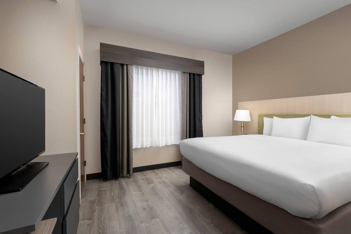 A hotel room with a large bed, a flat-screen TV, a desk with drawers, and a window with curtains.