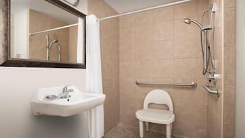 A bathroom with a white sink, a mirror, a shower with a handheld showerhead, and a grab bar.
