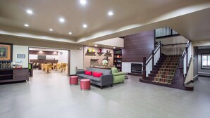 A spacious hotel lobby with a modern staircase, a seating area with a sofa and chairs, and a dining area in the background. - Country Inn & Suites by Radisson, Gainesville, FL (Gainesville)