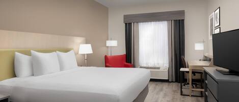 A hotel room with a large bed, a desk with a chair, a television, and a red chair.