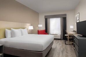 A hotel room with a large bed, a desk with a chair, a television, and a red chair.