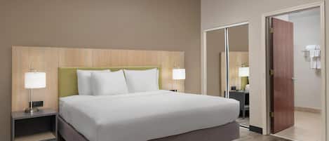A hotel room with a large bed, two bedside tables with lamps, a wooden headboard, and a door leading to a bathroom.