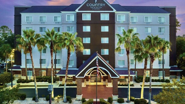 A multi-story hotel with a central entrance, palm trees, and a clear sky. - Country Inn & Suites by Radisson, Gainesville, FL (Gainesville)