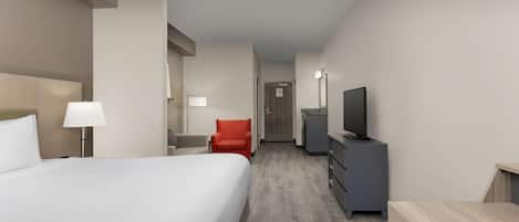 A hotel room with a large bed, a desk, a chair, a TV, and a dresser.