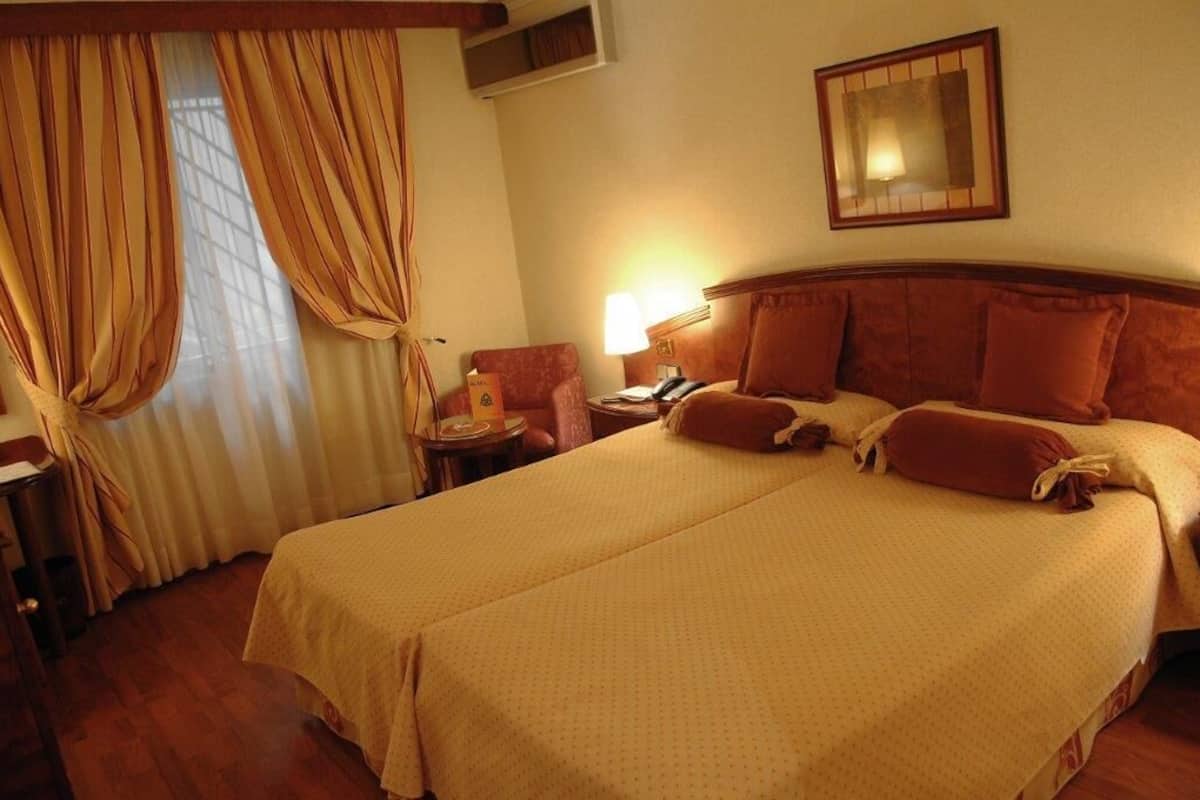A double bed with a wooden headboard, a bedside table with a lamp, and a chair.