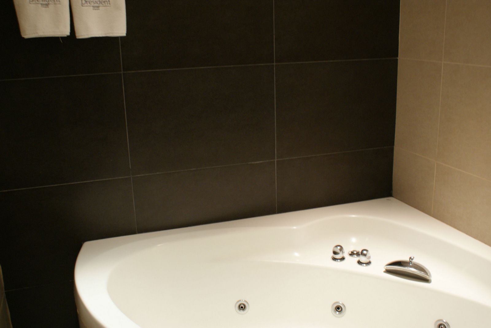 Ein Badezimmer mit einer weißen Badewanne, dunkel gefliesten Wänden und zwei Handtüchern, die an der Wand hängen.
