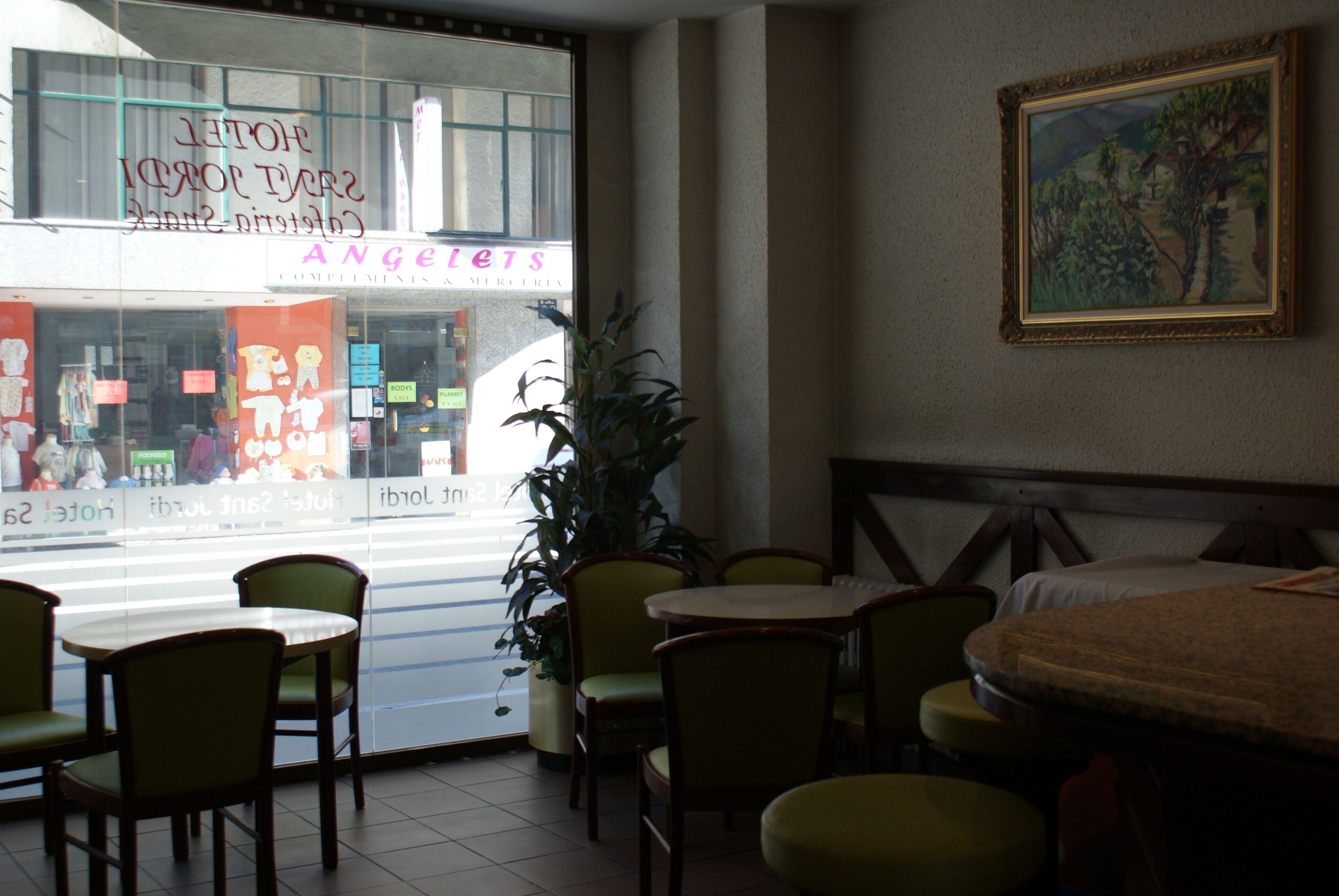 Habitació d'hotel amb una finestra gran, un quadre a la paret i diverses cadires i taules.
