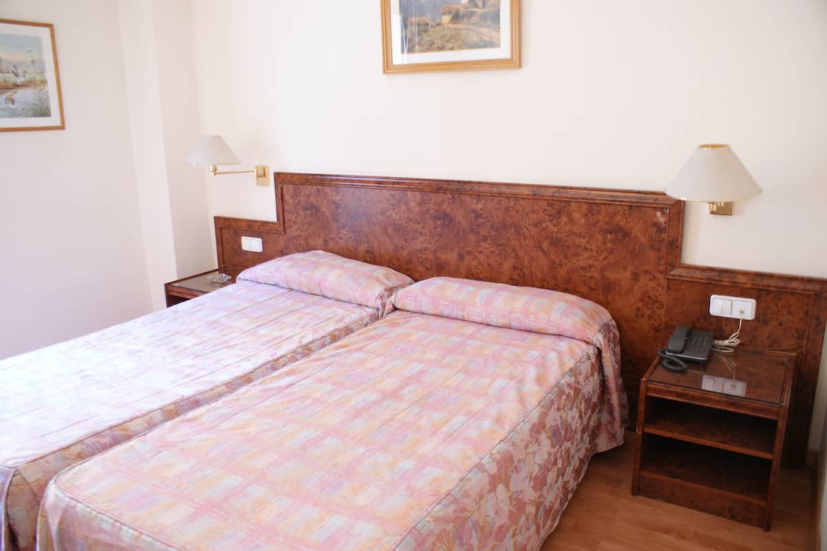 A double bed with a wooden headboard, two bedside tables with lamps, and a nightstand with a phone.