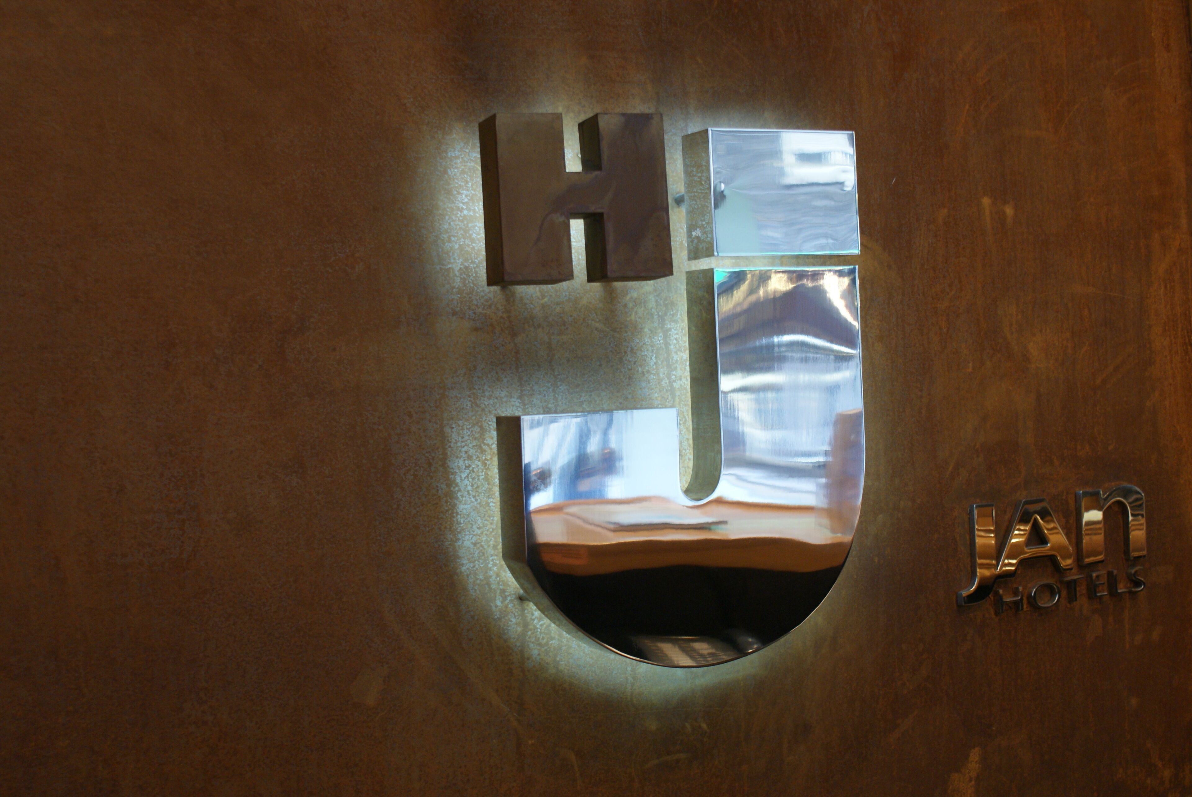 A metallic sign with the letters "H" and "J" for "Hotel" and "Jan Hotels" respectively, mounted on a wall.