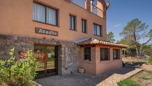 Ein Gebäude mit einer Steinfassade, einem Schild mit der Aufschrift 'Asador' und einem kleinen Zierbau aus Ziegeln mit einem gefliegelten Dach.