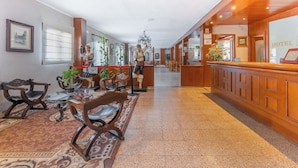 Eine Hotelhalle mit einer Rezeption, Holzstühlen, einem gemusterten Teppich und einer Chandelier.
