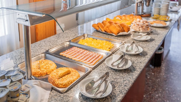 Ein Buffet mit verschiedenen Speisen, darunter Speck, Eier und Gebäck.