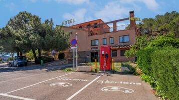 Hotel con zona de estacionamiento señalizada para carga de vehículos eléctricos, un letrero visible que indica 'No Estacionar' y un edificio con balcones.