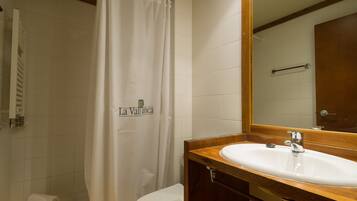 Un baño con cortina de ducha blanca, tocador de madera con lavabo y espejo.