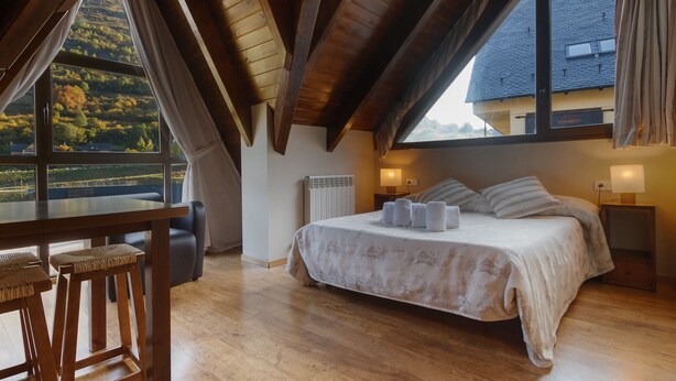 A bedroom with a large bed, a wooden table, and a view of the countryside. - Aparthotel La Vall Blanca (Vielha e Mijaran)