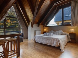 A bedroom with a large bed, a wooden table, and a view of the countryside.