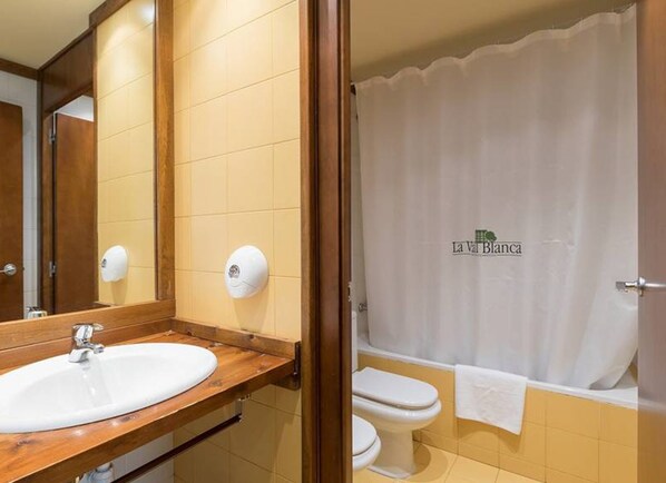 A bathroom with a wooden vanity, a sink, a mirror, a toilet, and a shower curtain.
