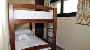 Una litera con ropa de cama blanca y una toalla enrollada.