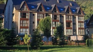 A multi-story building with a sloped roof, large windows, and a stone facade. - Aparthotel La Vall Blanca (Vielha e Mijaran)