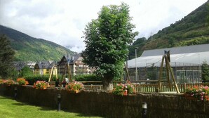 A garden with a large tree, a greenhouse, and traditional buildings in the background. - Aparthotel La Vall Blanca (Vielha e Mijaran)