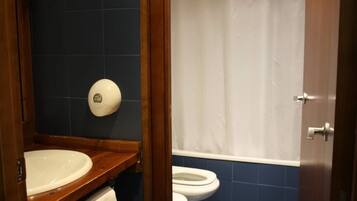 A bathroom with a wooden vanity, a white sink, a toilet, and a shower curtain.