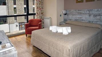 A bedroom with a large bed, a red plaid armchair, a radiator, and a window with a view of a building.