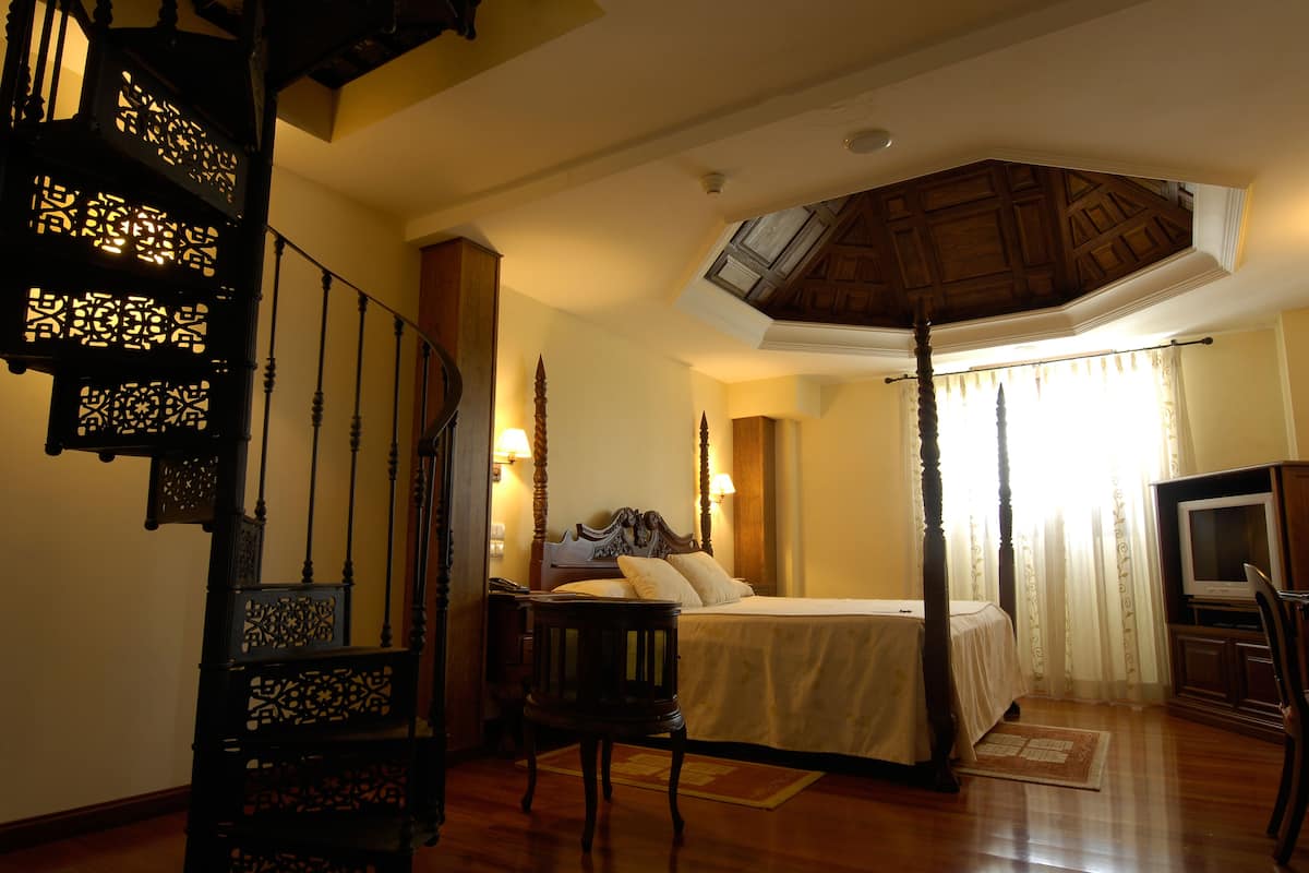 Ein Schlafzimmer mit Himmelbett, Fernseher und einer Treppe mit aufwendiger Holzvertäfelung.