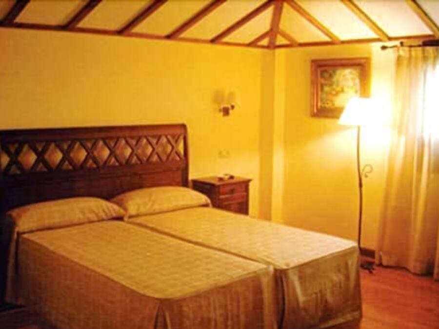 A double bed with a wooden headboard, a bedside table, and a lamp.