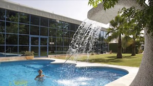 A swimming pool with a waterfall feature, surrounded by a modern building with large windows. - Hotel Domus Selecta Finca Eslava (Antequera)