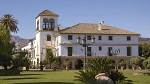 A large white building with a bell tower, surrounded by well-maintained gardens and palm trees. - Hotel Domus Selecta Finca Eslava (Antequera)