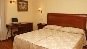 A hotel room with a wooden bed, a desk with a laptop, and two wall-mounted lamps.