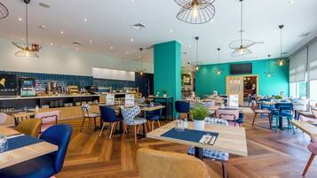 Een modern restaurant met houten vloeren, wanden in blauwgroen en verschillende zitmogelijkheden, zoals tafels en stoelen.