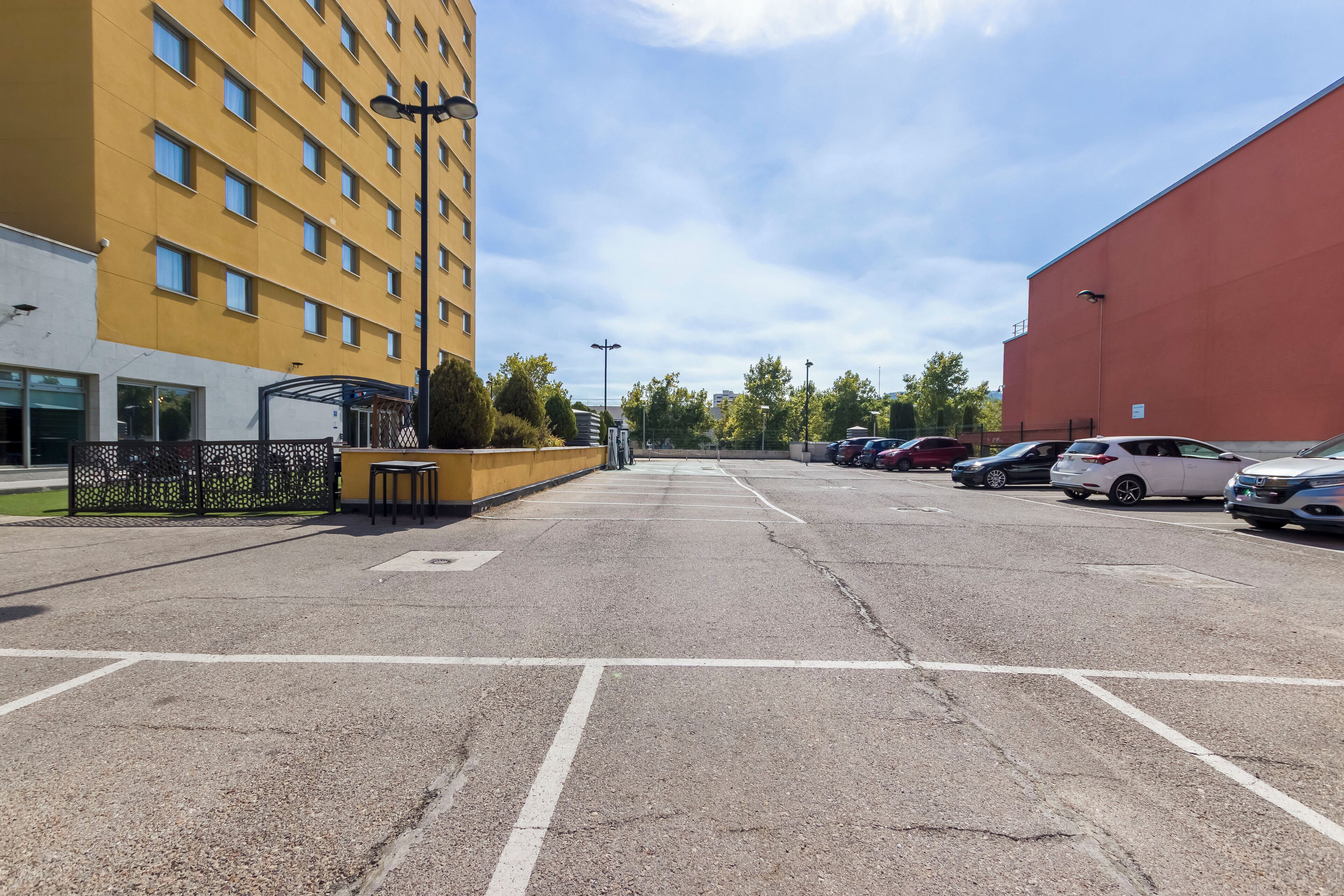 Een parkeerplaats met meerdere auto's, een geel gebouw en een rood gebouw op de achtergrond.