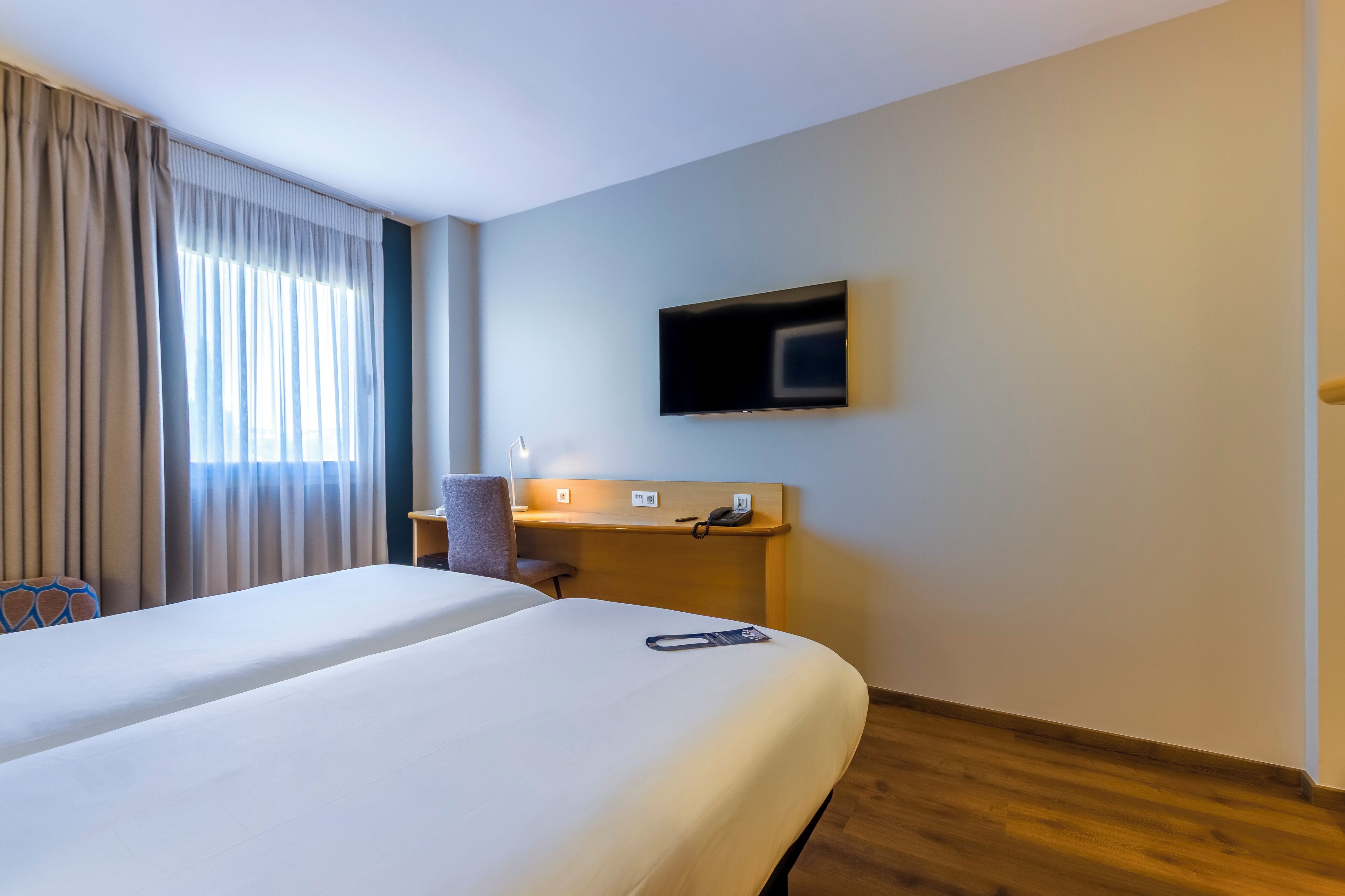 Een hotelkamer met twee bedden, een bureau met telefoon en een televisie aan de muur.