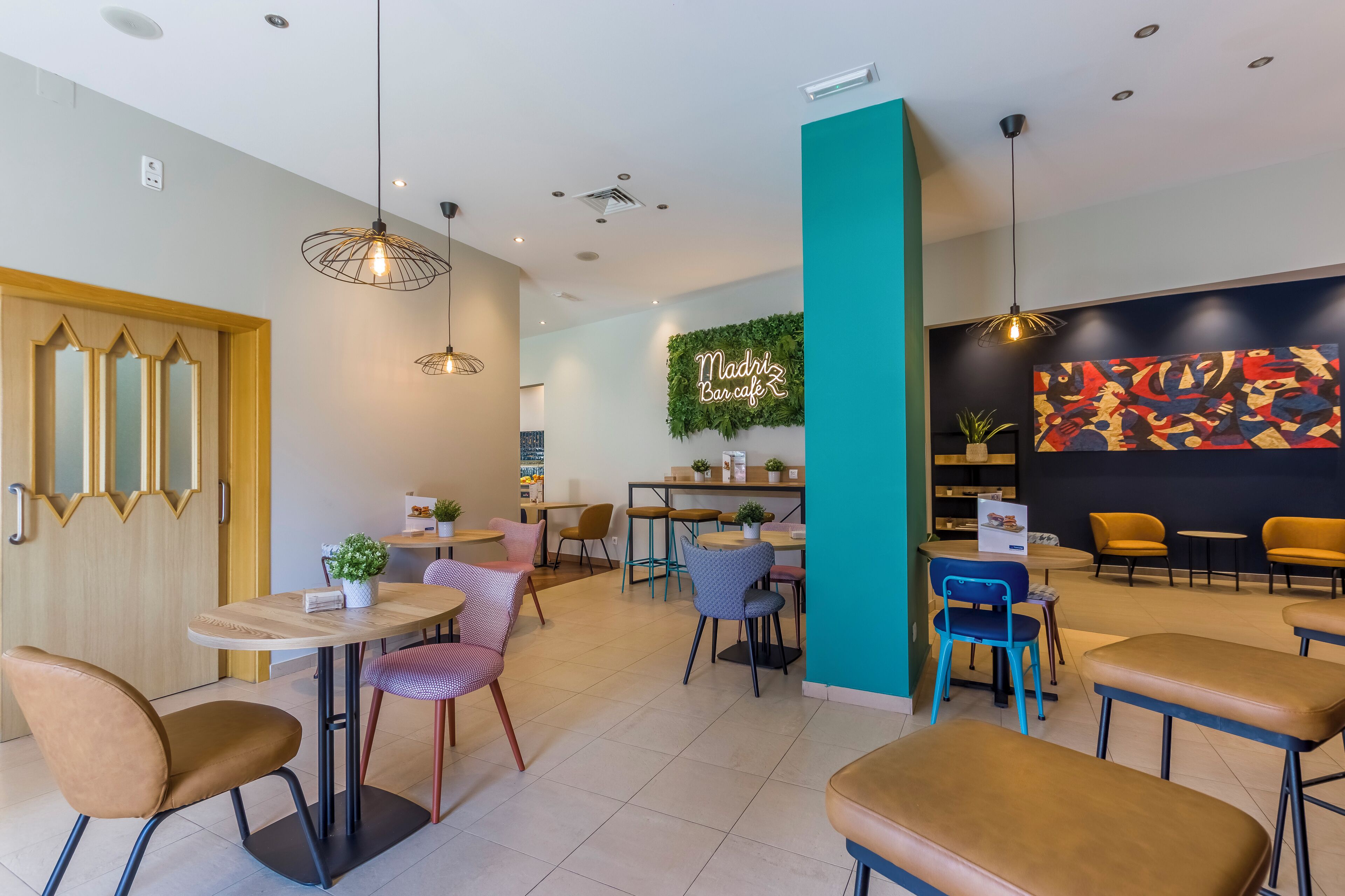 Un café moderno con diversas opciones de asientos, incluyendo mesas y sillas, y una llamativa obra de arte en la pared.