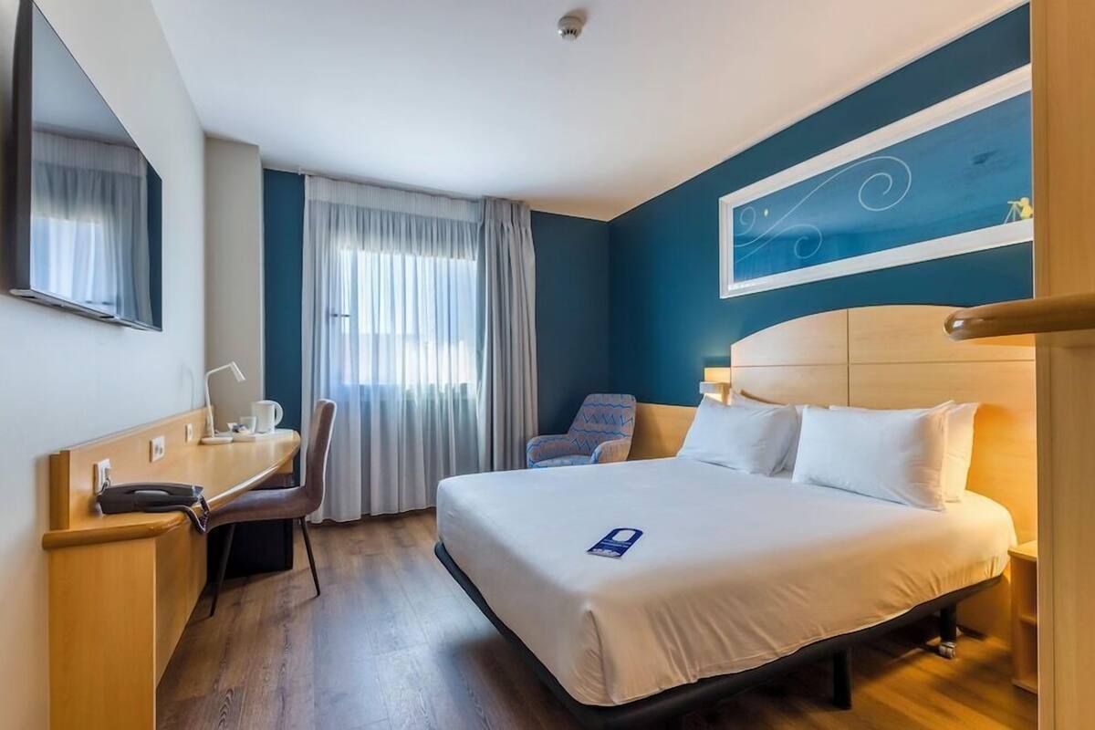 A hotel room with a bed, a desk, a chair, and a window with curtains.