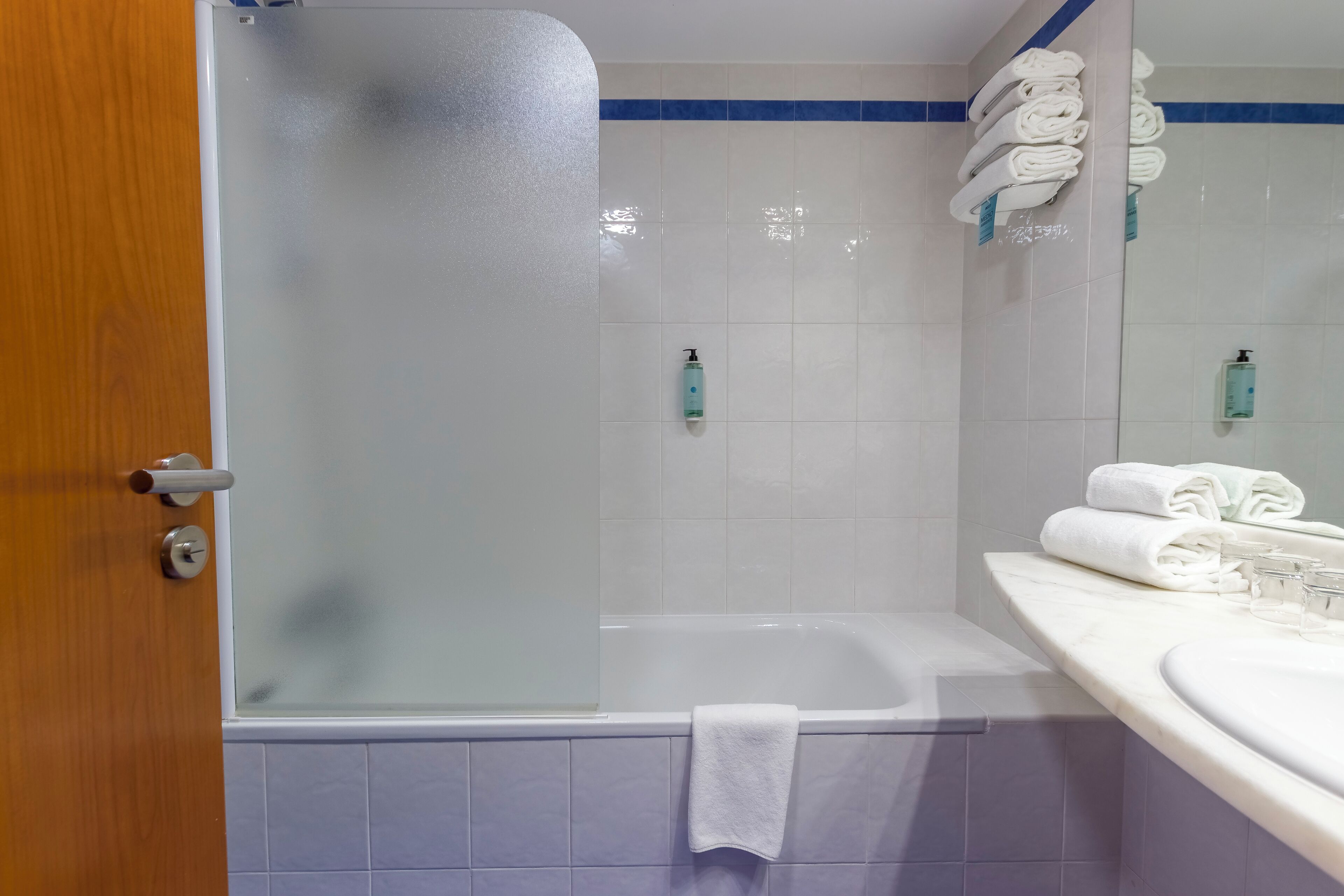 Een badkamer met een douchecabine van glas, een wit bad en een wastafel met spiegel.