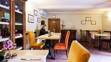 Restaurante com várias mesas e cadeiras, um armário de madeira com portas de vidro e uma porta com um letreiro.