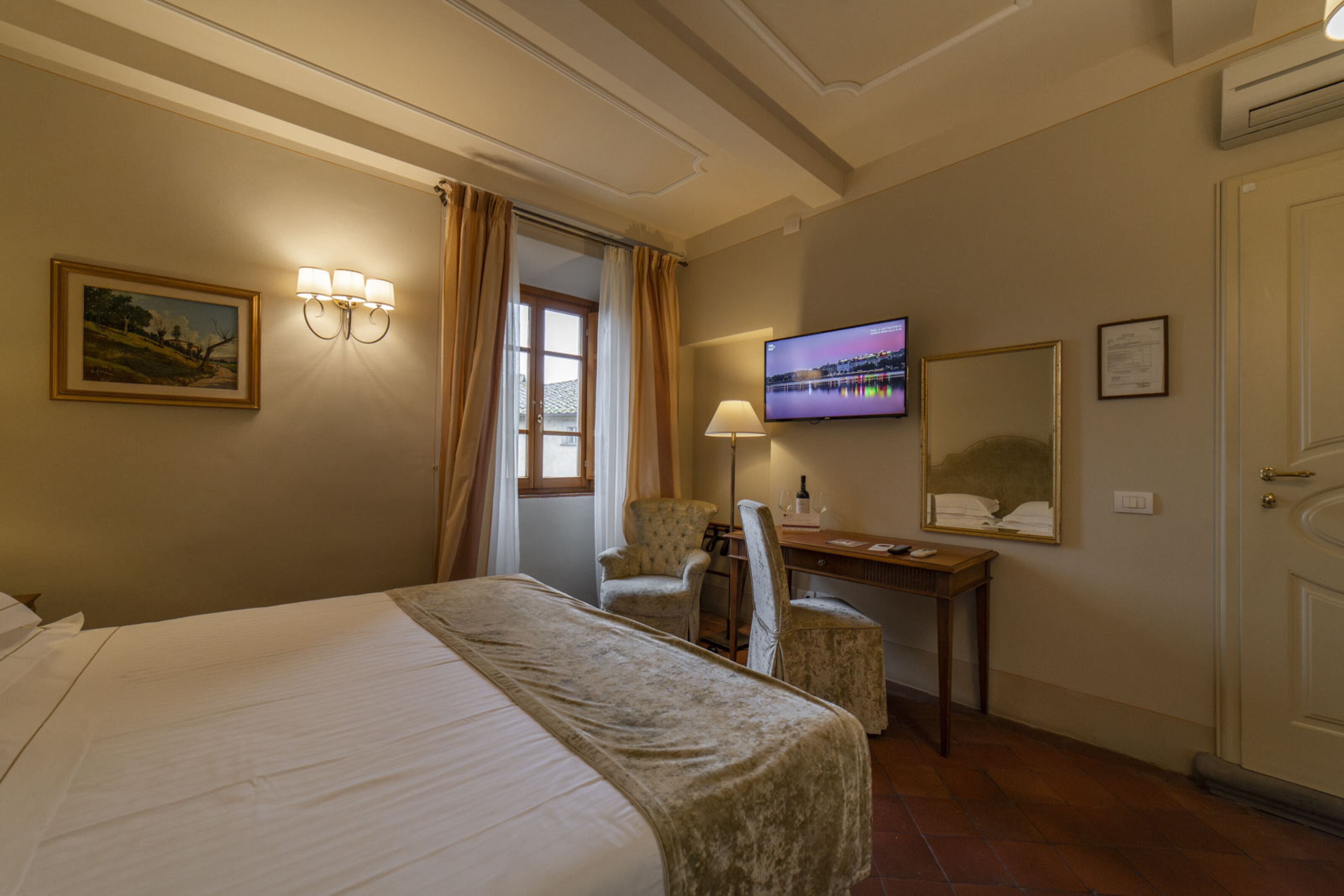 Una habitación de hotel con cama, escritorio con silla, televisor y espejo.