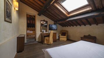Un dormitorio con tragaluces, vigas de madera, una cama, un escritorio, una silla y un televisor.