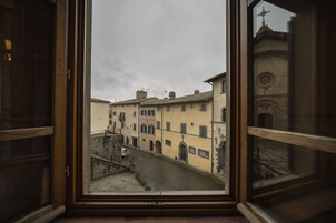 A view through a window of a narrow street with buildings, a clock tower, and a small bridge.