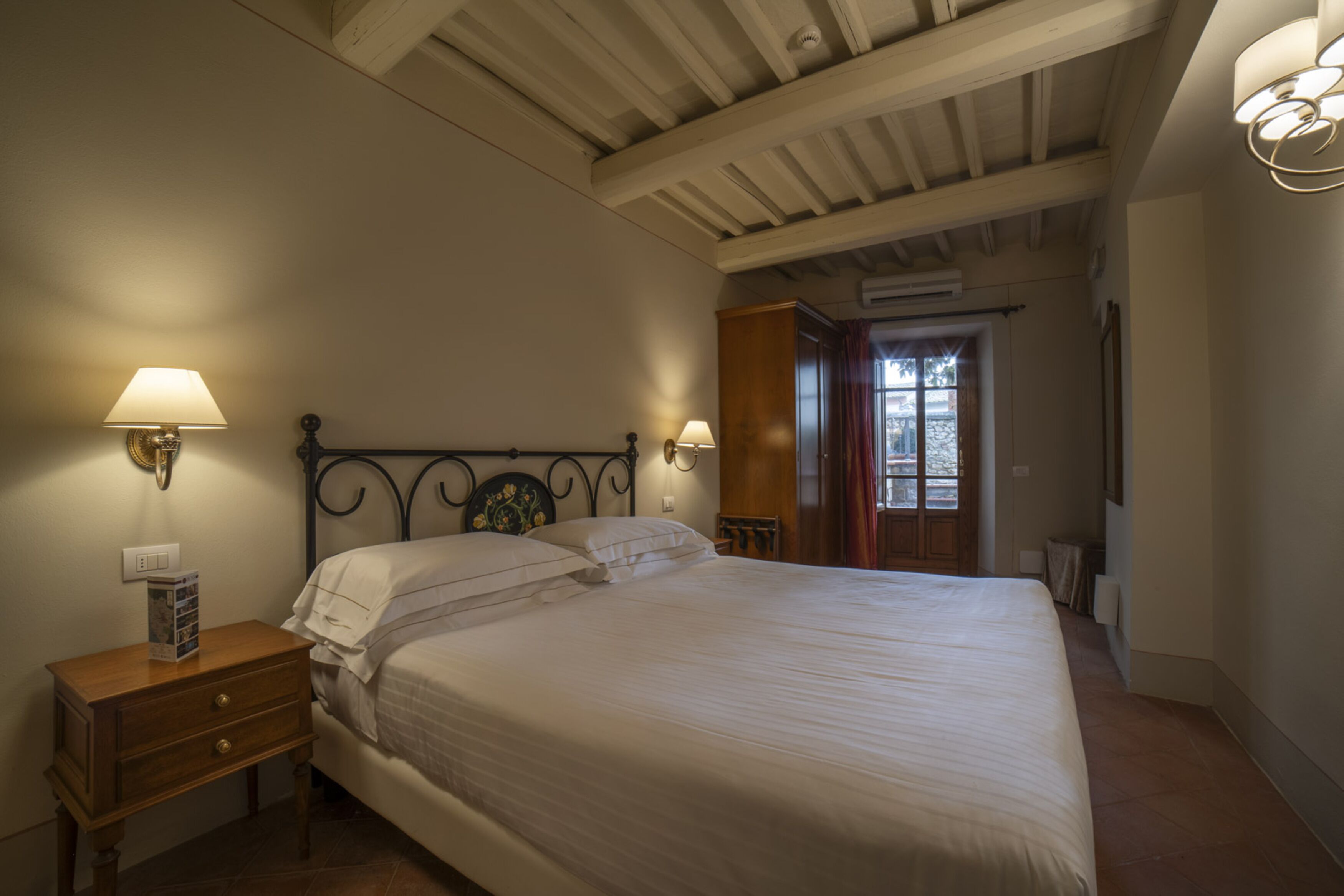 A bedroom with a bed, nightstand, wall-mounted lamps, and a wooden wardrobe.