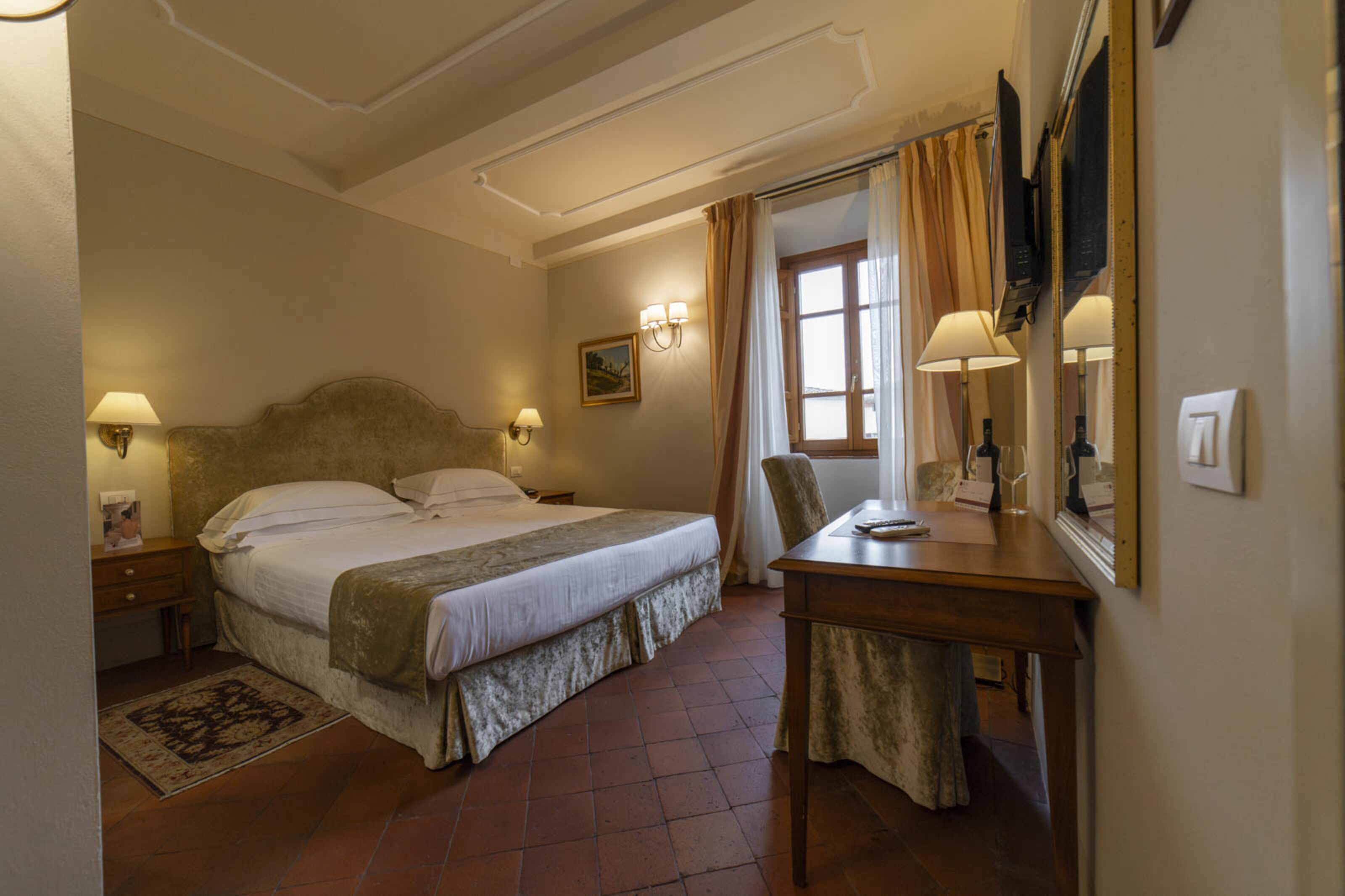 Una habitación de hotel con una cama, lámparas de noche, un escritorio y una ventana con cortinas.