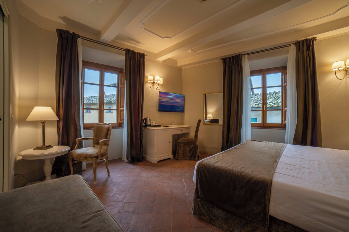 A hotel room with two beds, a desk, a chair, a lamp, and a painting on the wall.