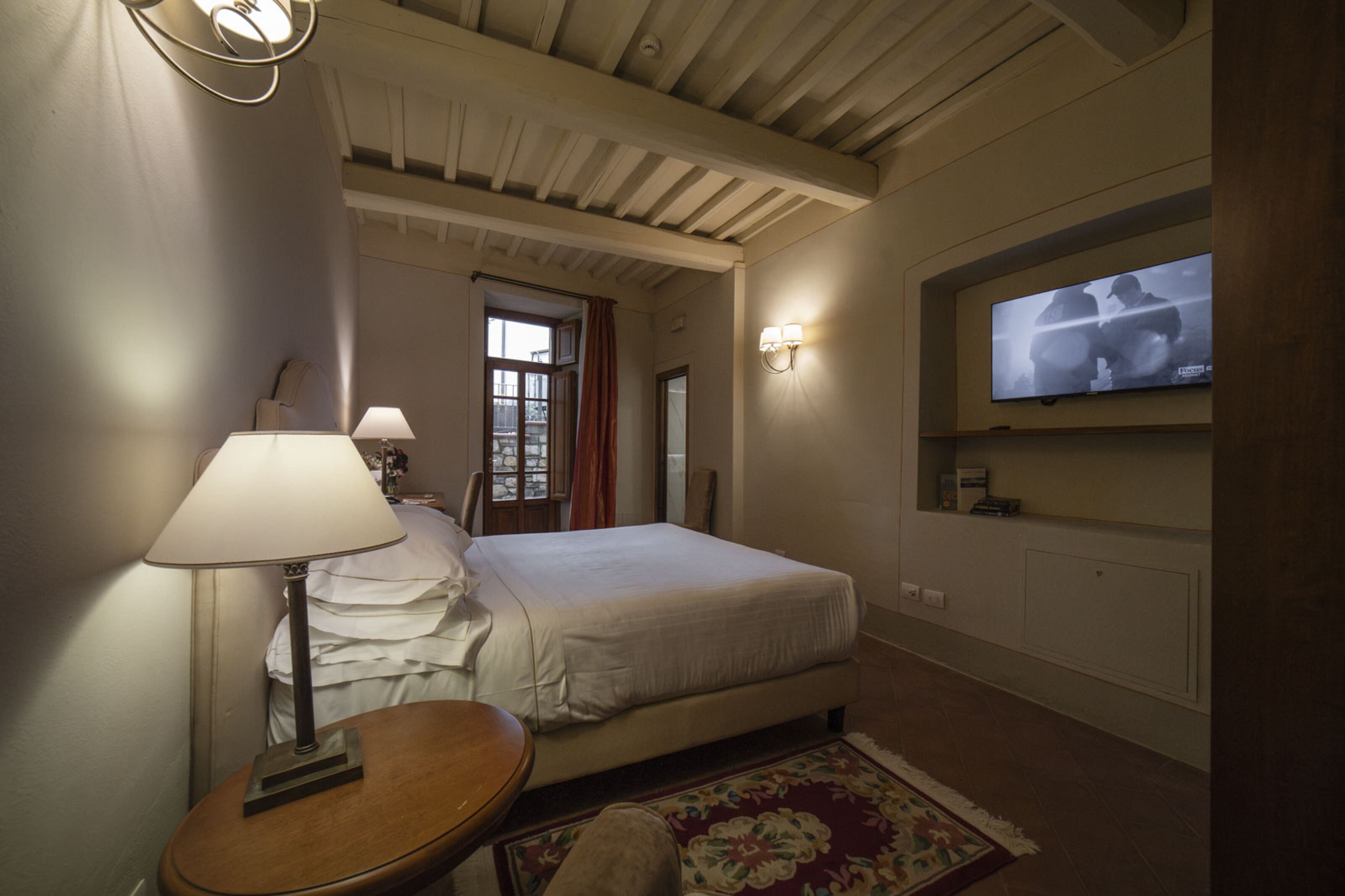 Una habitación de hotel con una cama, un televisor montado en la pared, una lámpara y una mesita.