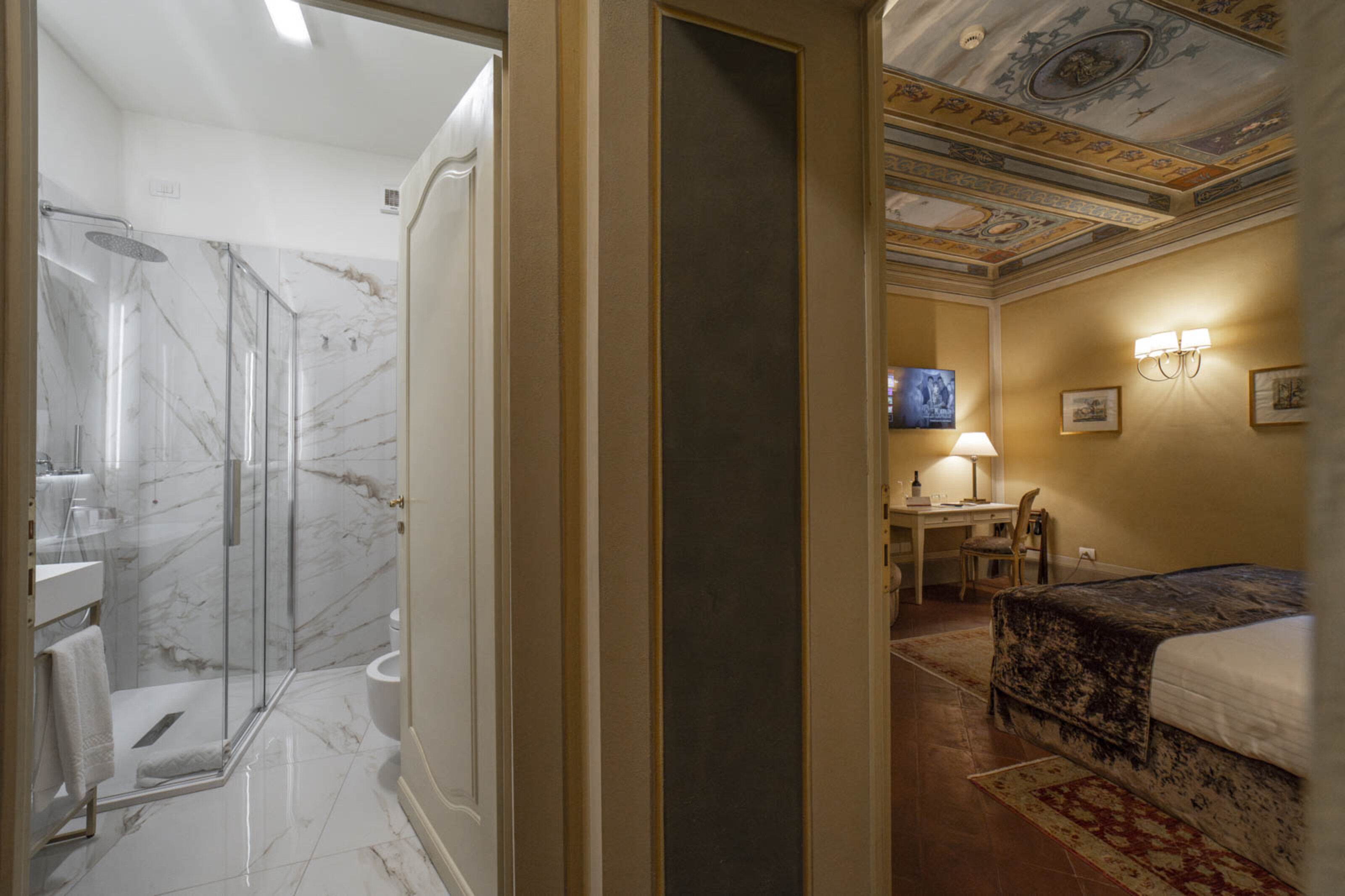 Una camera d'albergo con doccia vetrata, un letto, una scrivania con sedia e televisore.